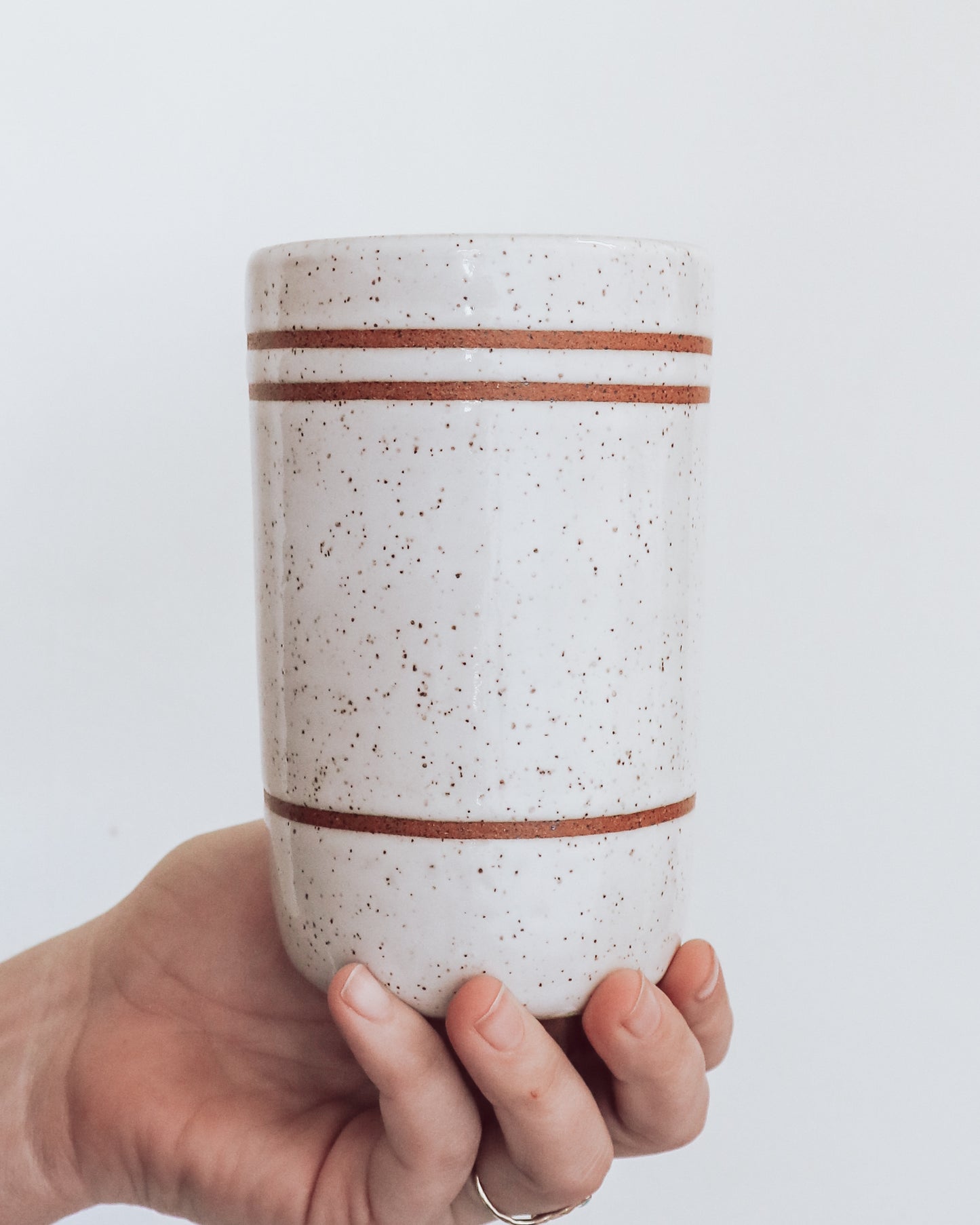 Back of tumbler showing three stripes on white glaze held in a person's hand against a white background.