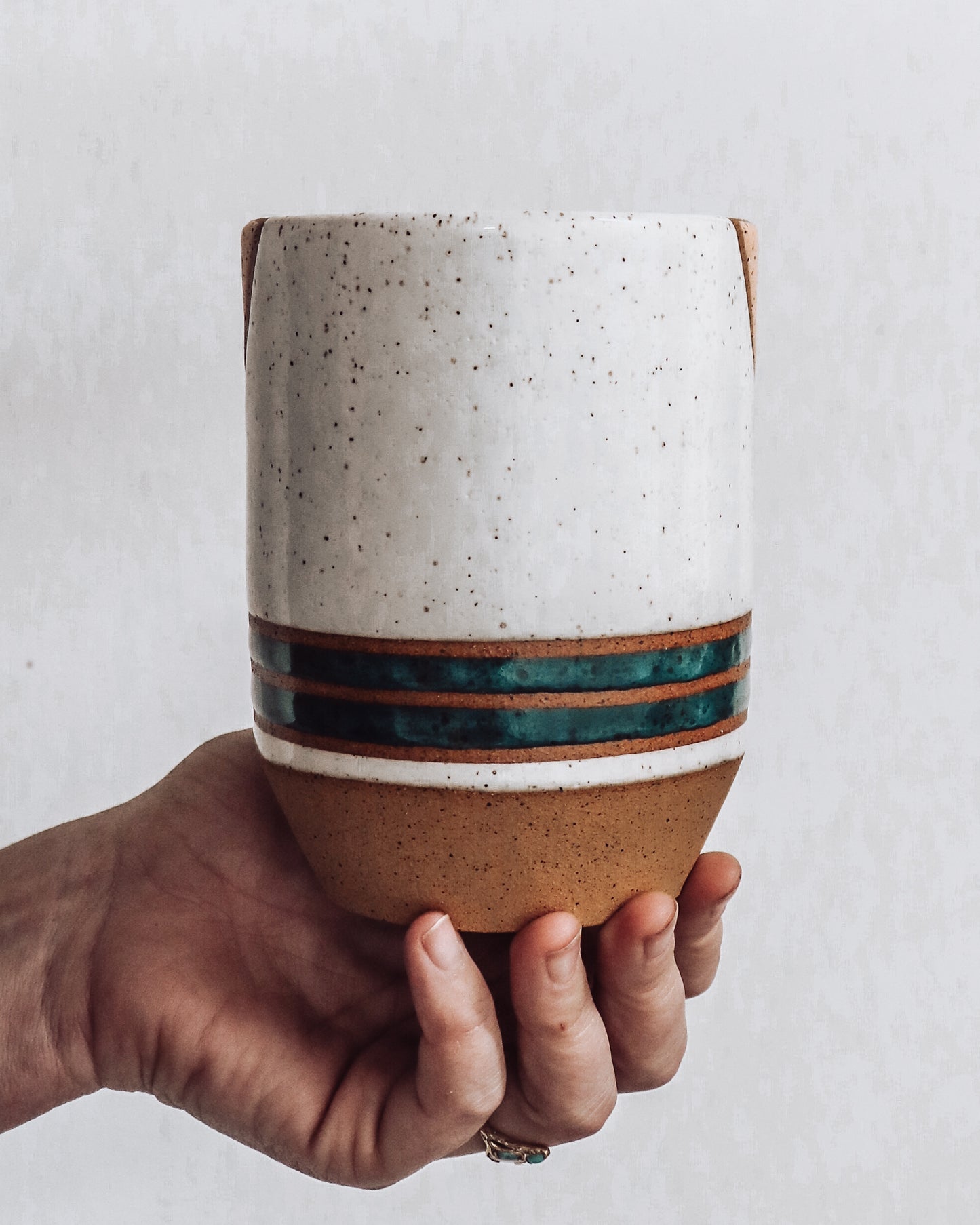 hand holding a handmade ceramic vase (back view) featuring teal stripes and  white top.