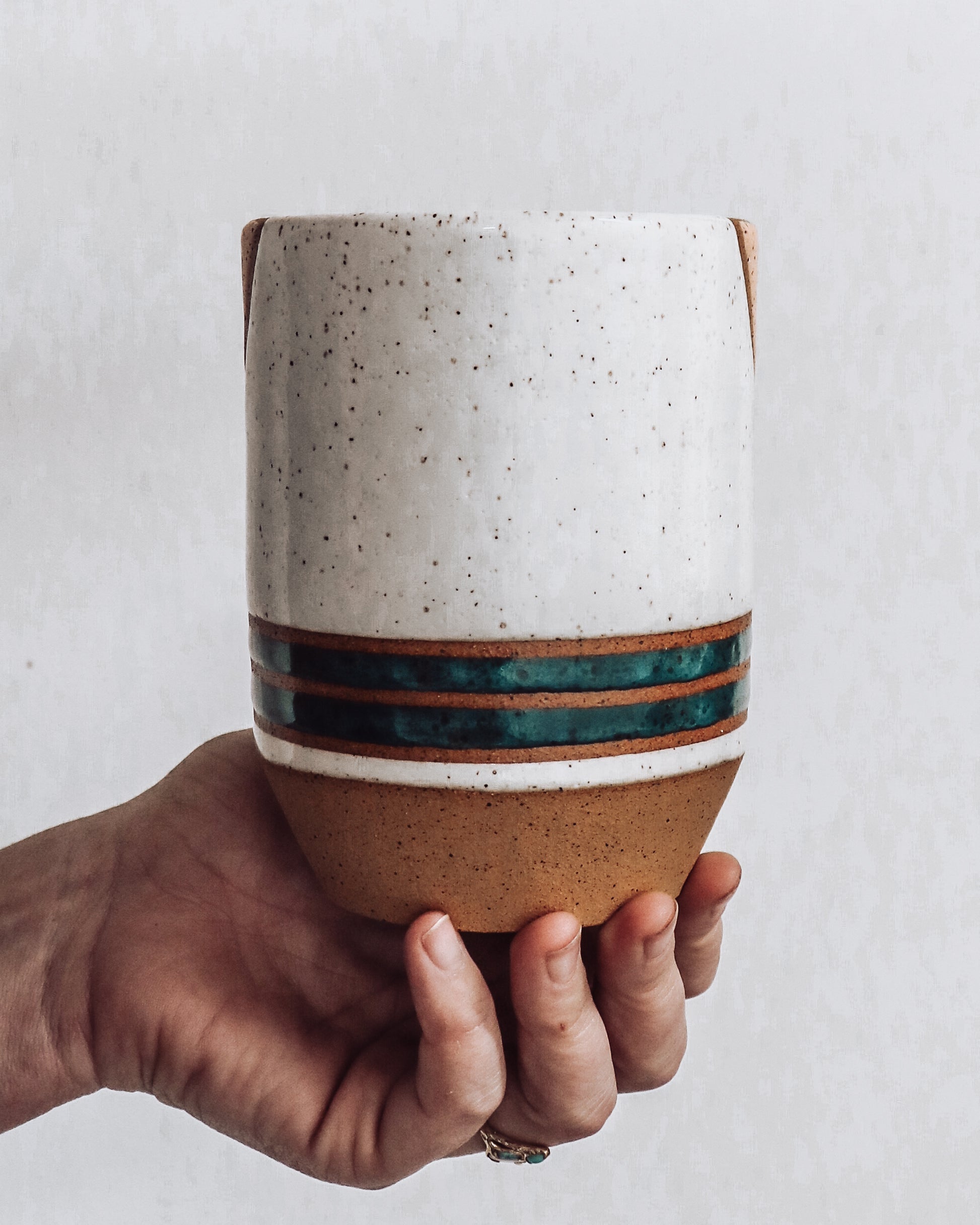 hand holding a handmade ceramic vase (back view) featuring teal stripes and  white top.