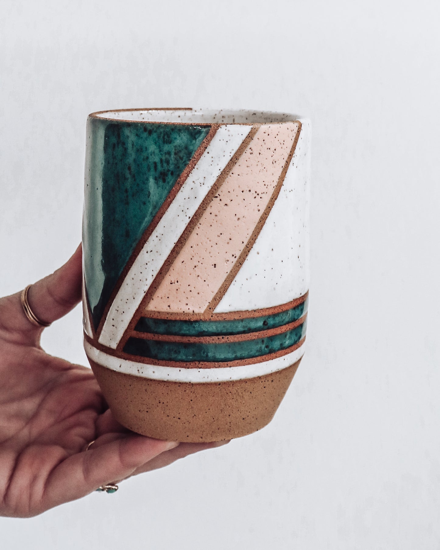 hand holding a handmade ceramic vase (side view) featuring teal, white and pink glaze with geometric pattern.