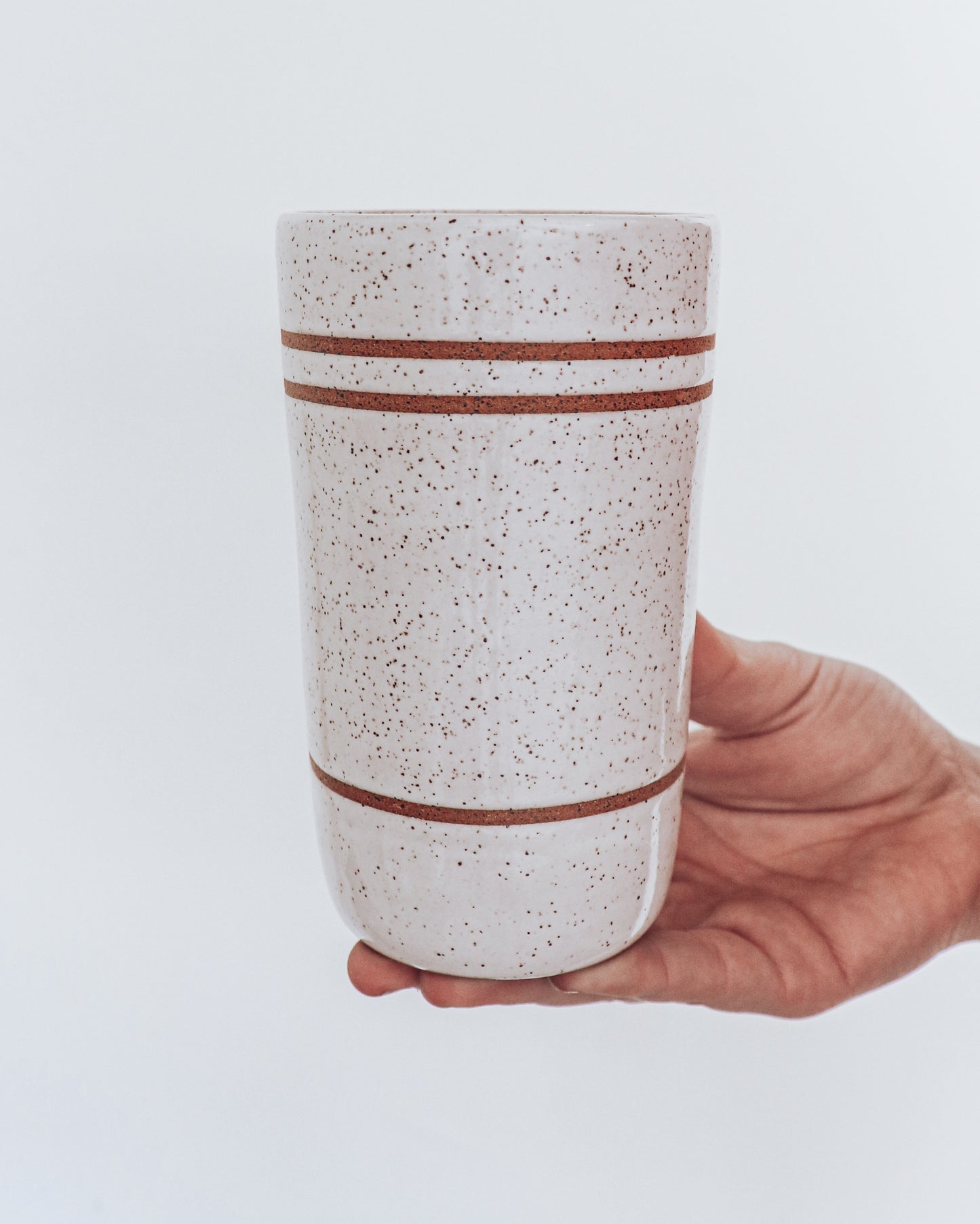 A ceramic tumbler showing three steps on  glossy white glaze, held in a person's hand against a white background.