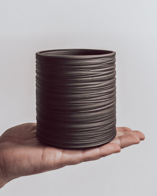 hand holding a handmade dark ceramic planter with horizontal textured ridges. 