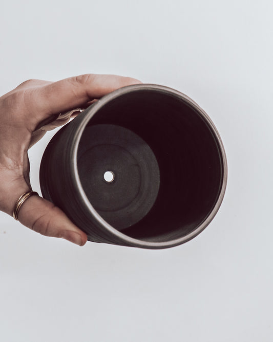 hand holding a handmade dark ceramic planter with horizontal textured ridges. shows interior of planter is unglazed.