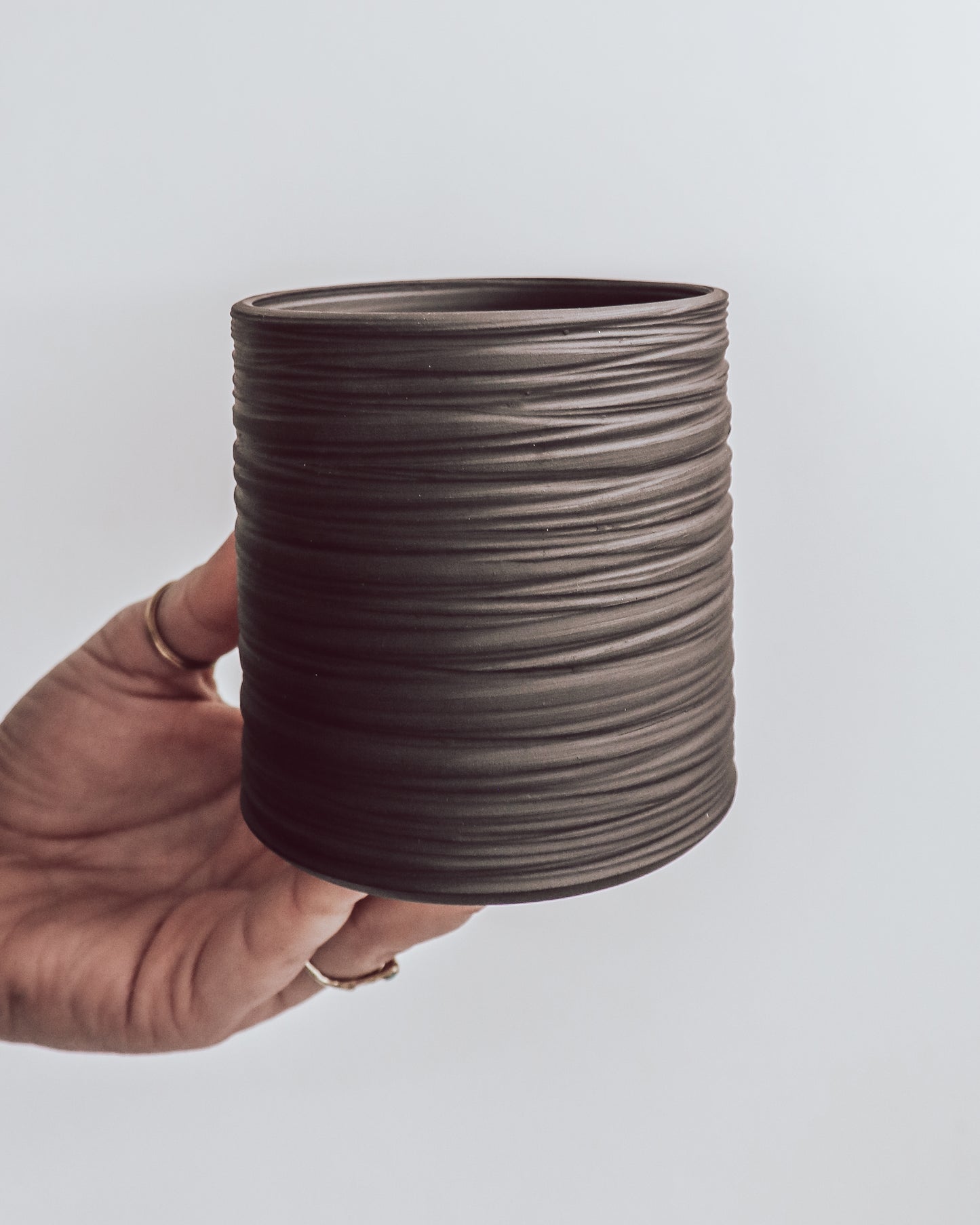 hand holding a handmade dark ceramic planter with horizontal textured ridges. 