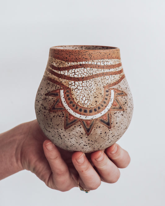 A hand holding a small brown and beige ceramic vase with a crackled texture and geometric patterns.