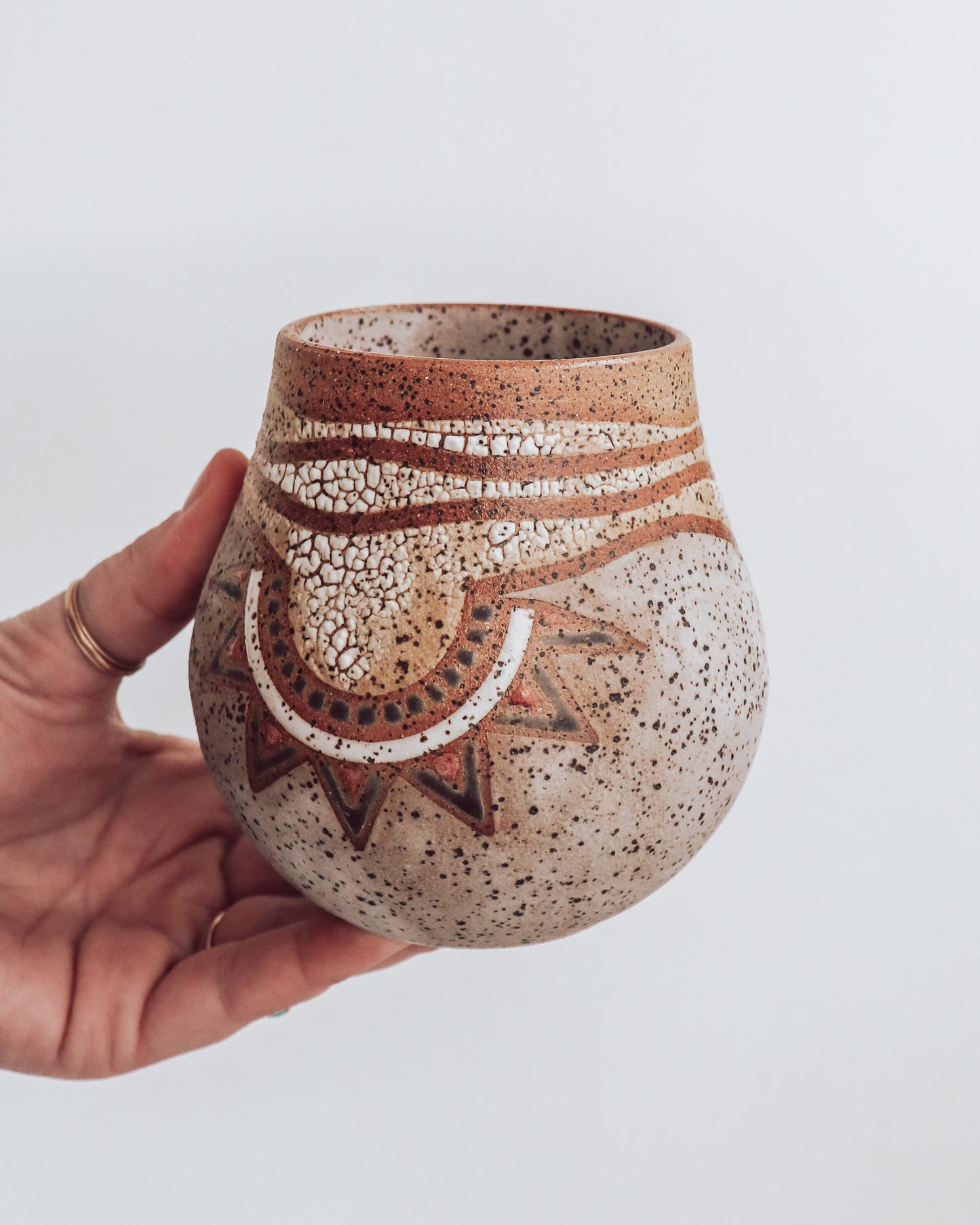 A hand holding a small brown and beige ceramic vase with a crackled texture and geometric patterns.
