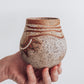 A hand holding a small brown and beige ceramic vase with a crackled texture and geometric patterns.