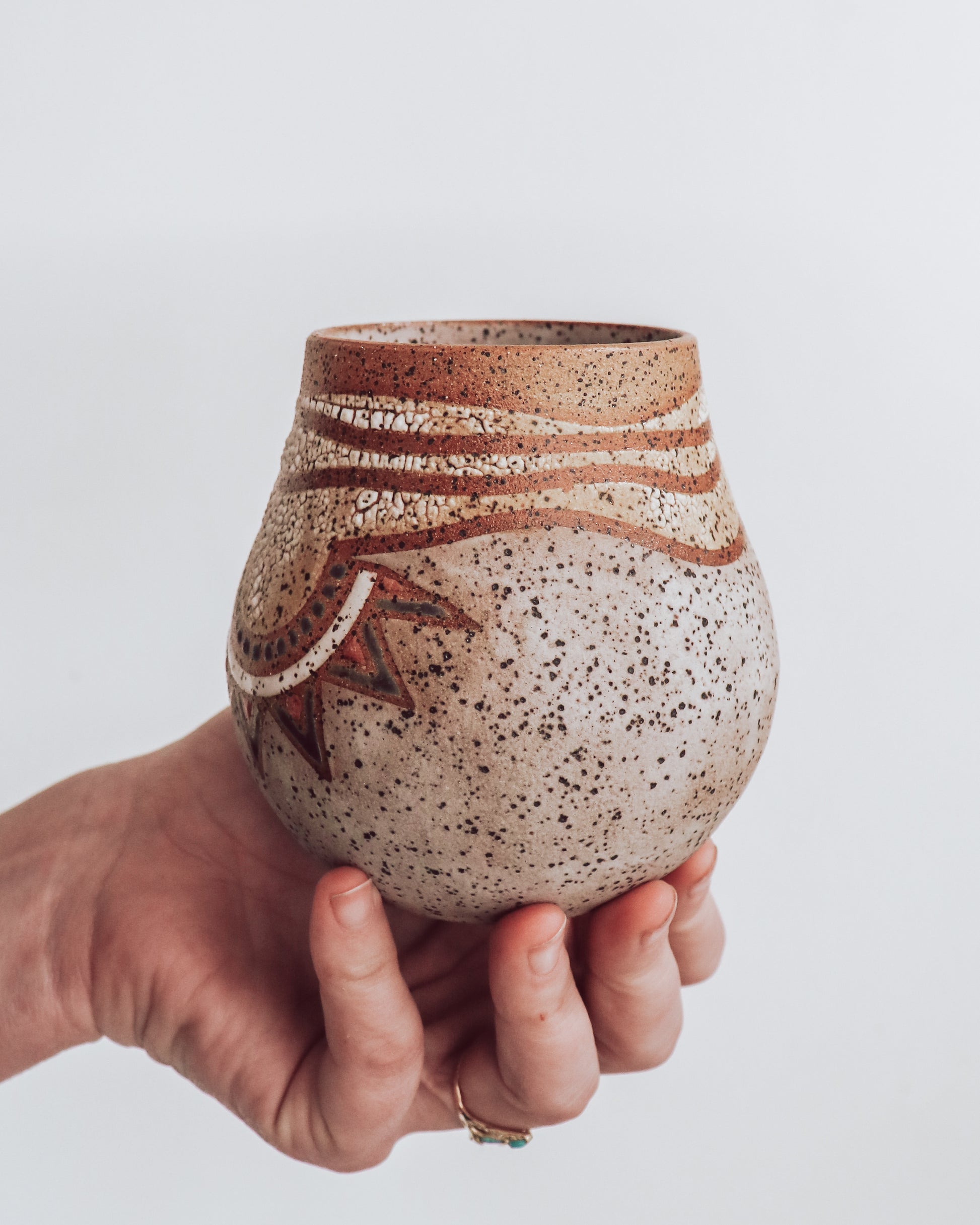 A hand holding a small brown and beige ceramic vase with a crackled texture and geometric patterns.