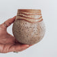 A hand holding a small brown and beige ceramic vase with a crackled texture and geometric patterns.
