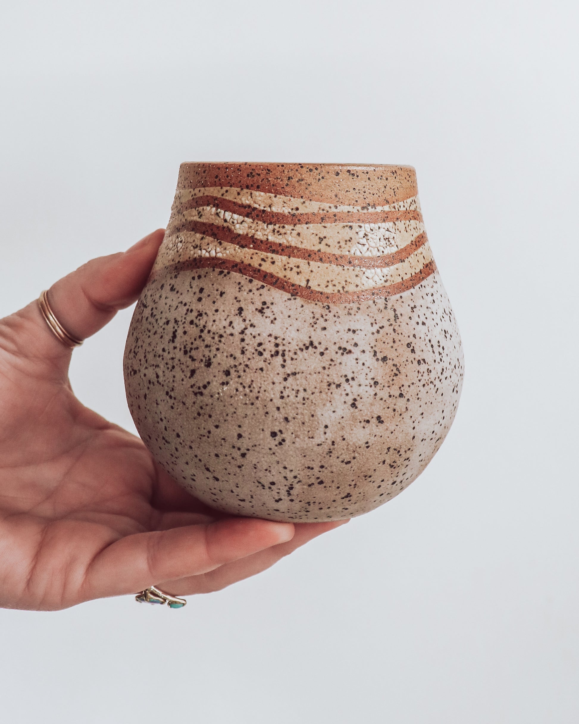A hand holding a small brown and beige ceramic vase with a crackled texture and geometric patterns.