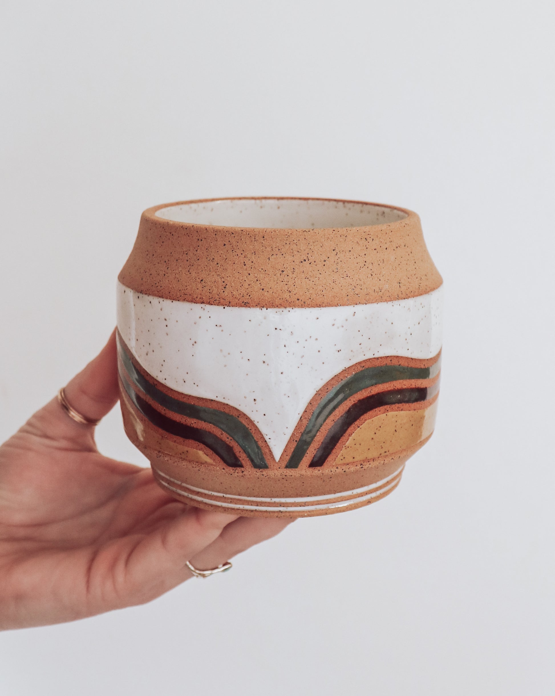 Hand holding a handmade ceramic planter with white glaze and wavy multicolored stripe detailing. 