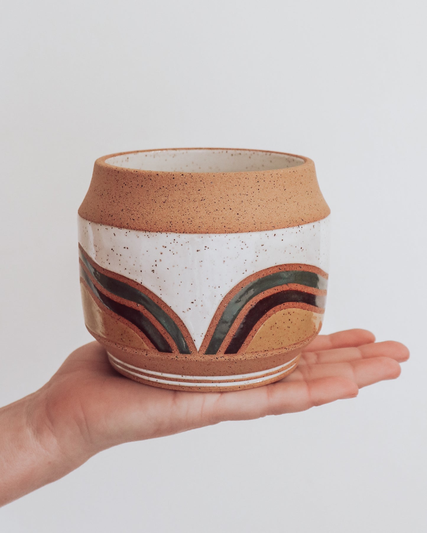 Hand holding a handmade ceramic planter with white glaze and wavy multicolored stripe detailing. 