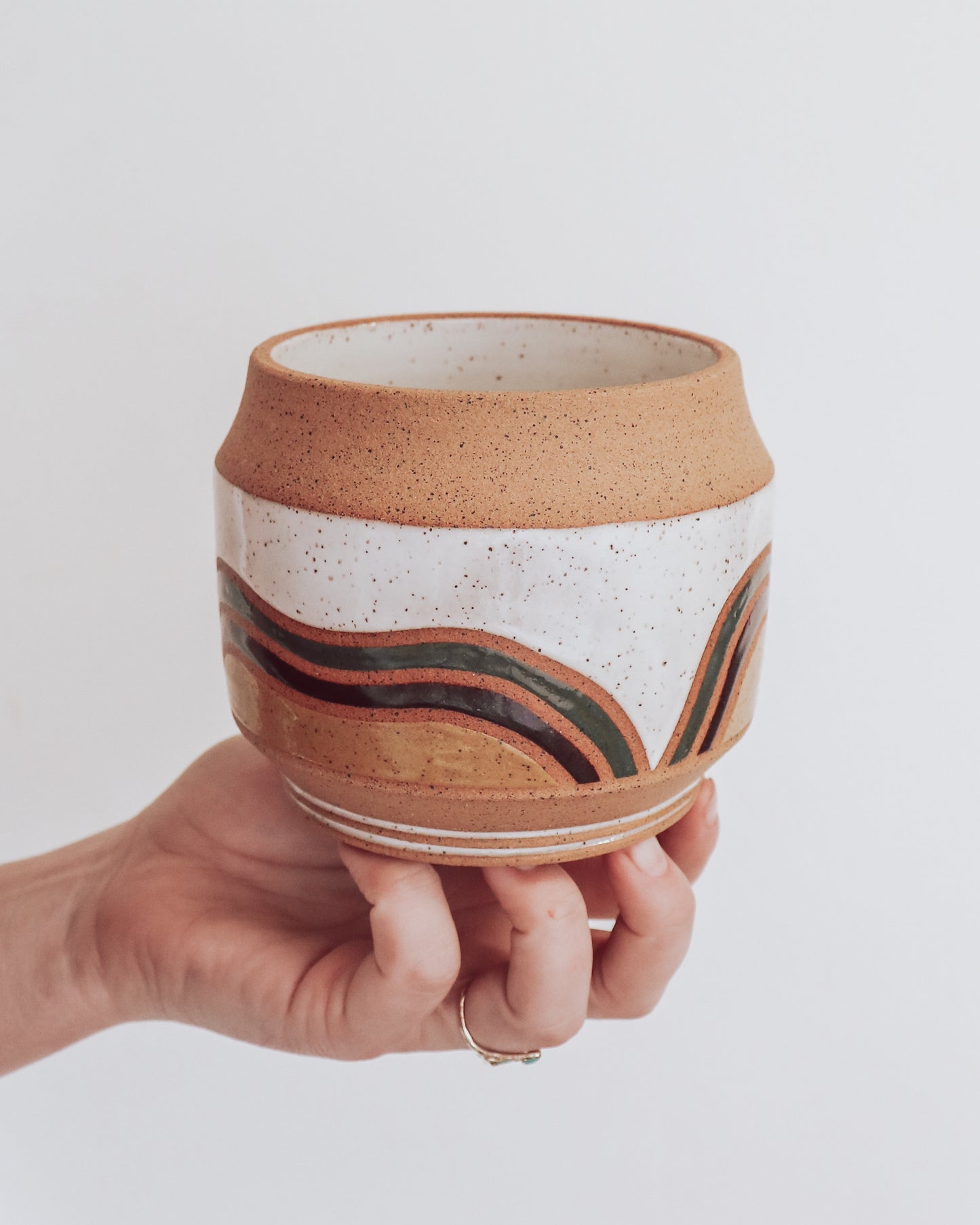 Hand holding a handmade ceramic planter with white glaze and wavy multicolored stripe detailing. 