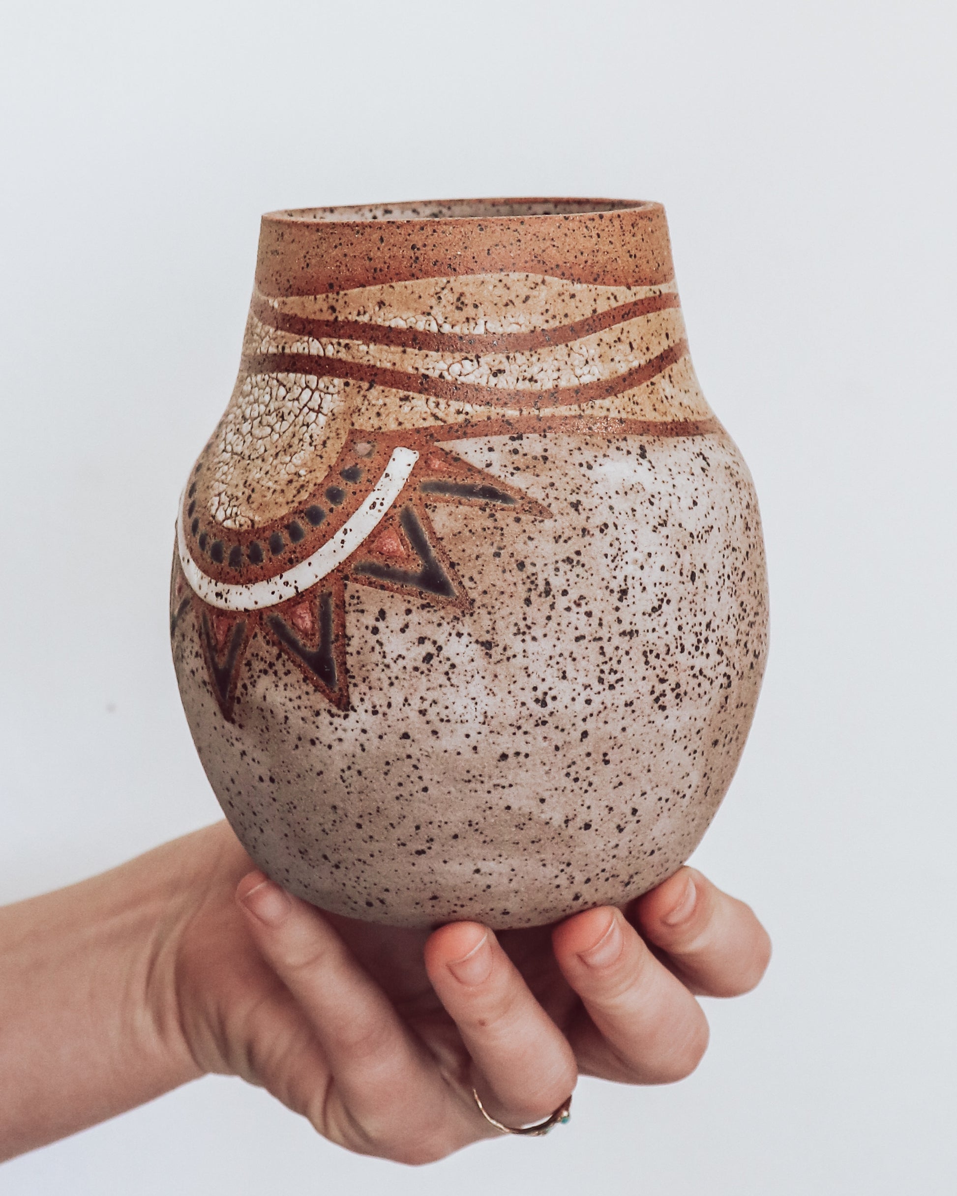 A hand holding a small brown and beige ceramic vase with a crackled texture and geometric patterns.