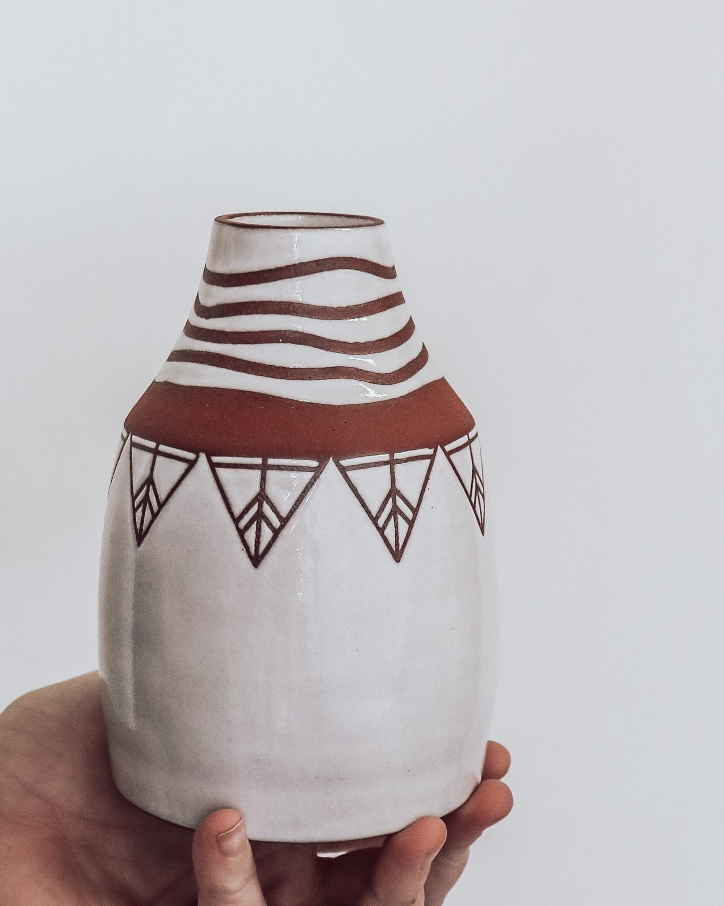 Hand holding handmade terra cotta vase with white geometric glaze patterns. 