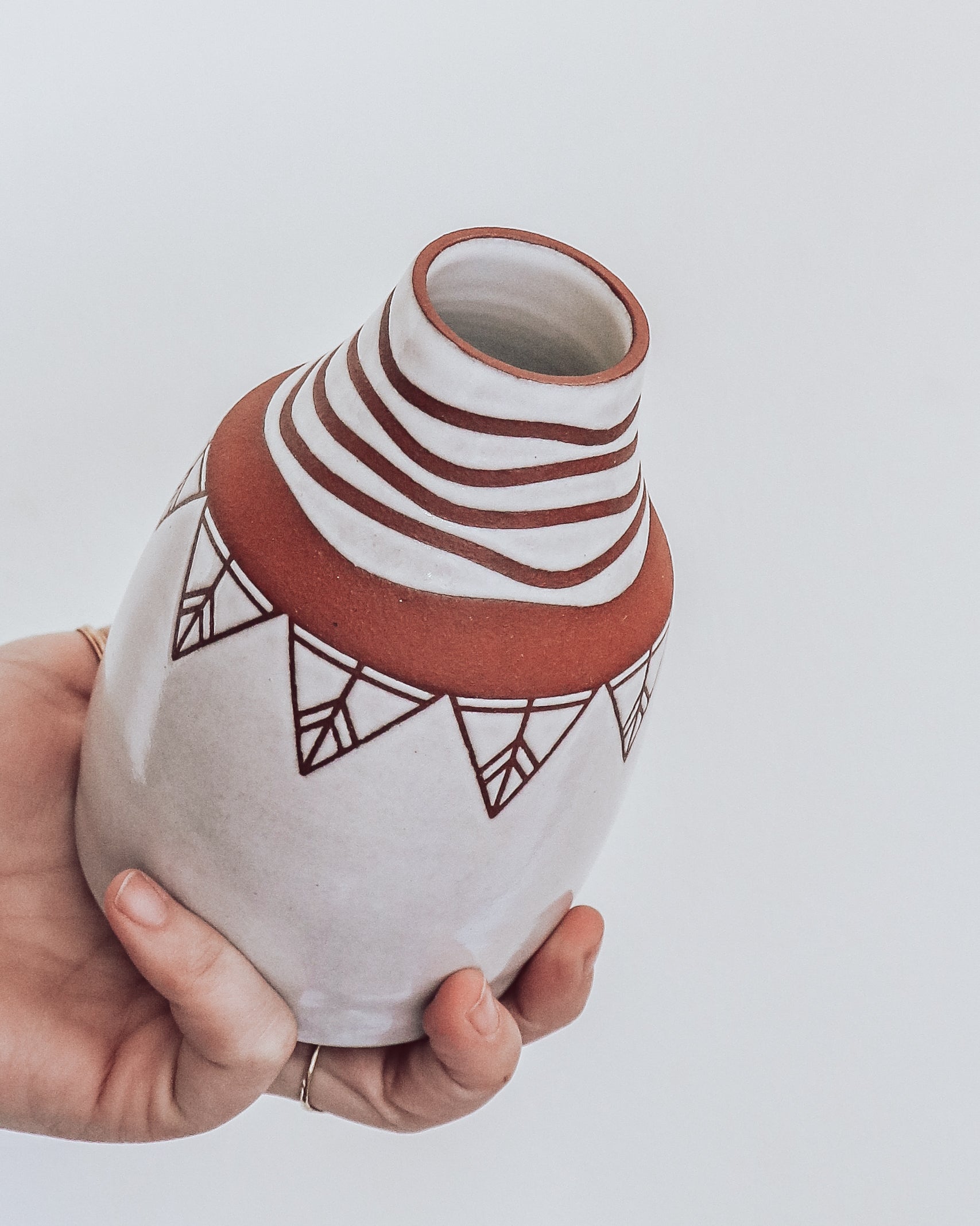 Hand holding handmade terra cotta vase with white geometric glaze patterns. 